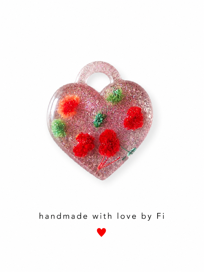 Red and orange dried flower resin heart pendant with pink glitter base and green botanical sprigs handmade by Fi