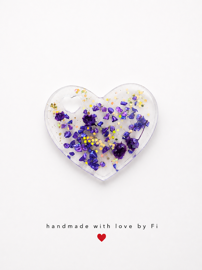 Clear resin heart pendant filled with purple amethyst chips, dried flower, holographic glitter and gold sequins handmade by Fi